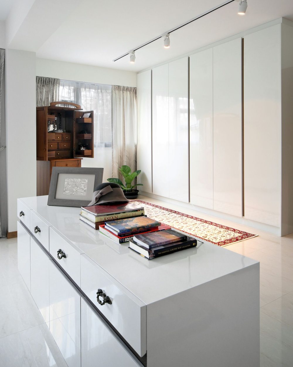 A vintage wooden jewellery cabinet adds a personal, heirloom touch to the bedroom, set against glossy white wardrobes and a patterned runner.
