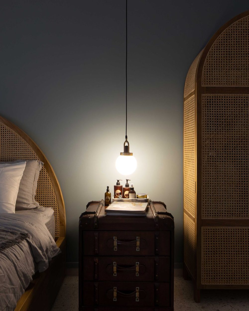 A rounded cane headboard and a vintage leather trunk nightstand give the bedroom a relaxed, collected character.