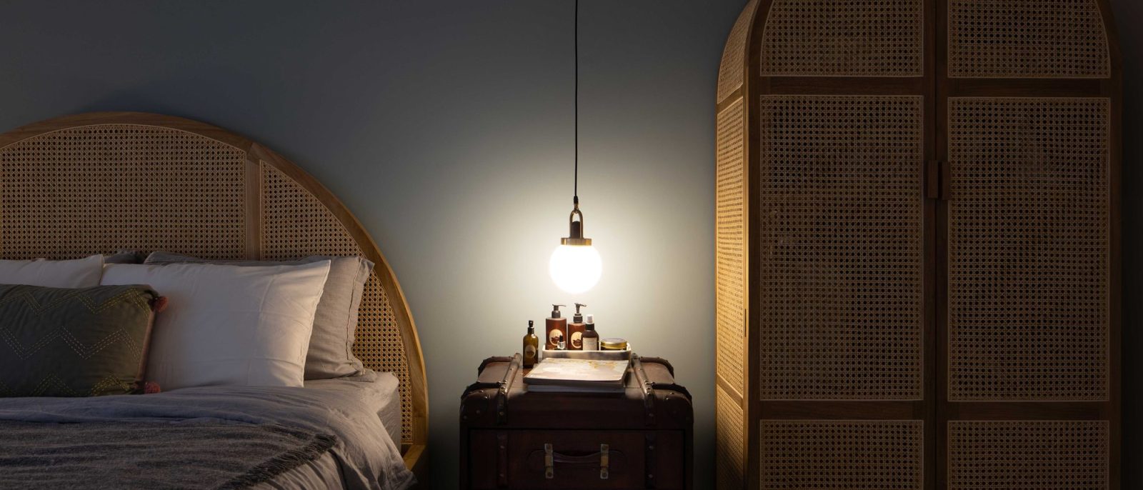 A rounded cane headboard and a vintage leather trunk nightstand give the bedroom a relaxed, collected character.