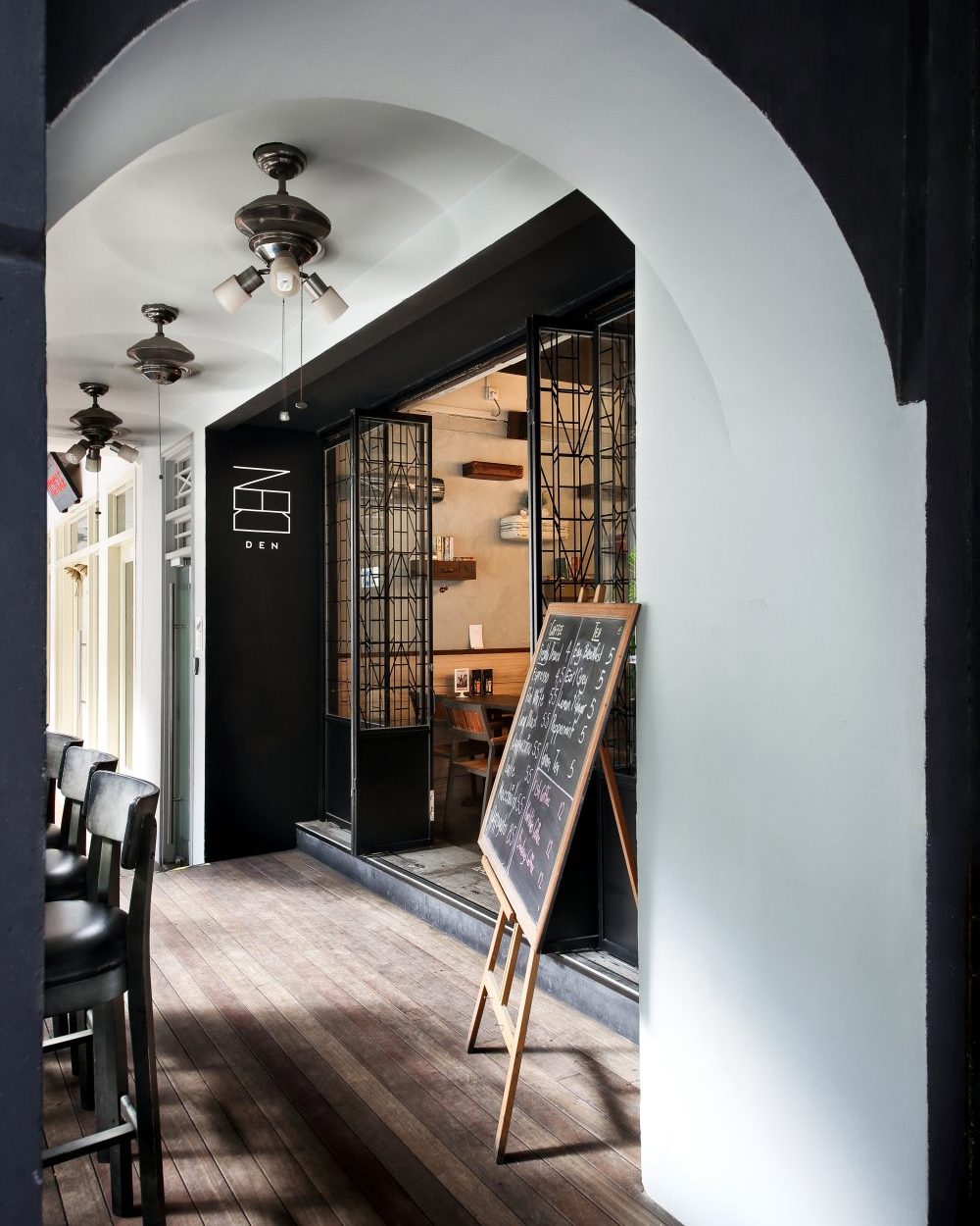 A geometric glass-and-steel door and minimalist wordmark signage announce the bar's entrance beneath a plastered archway.