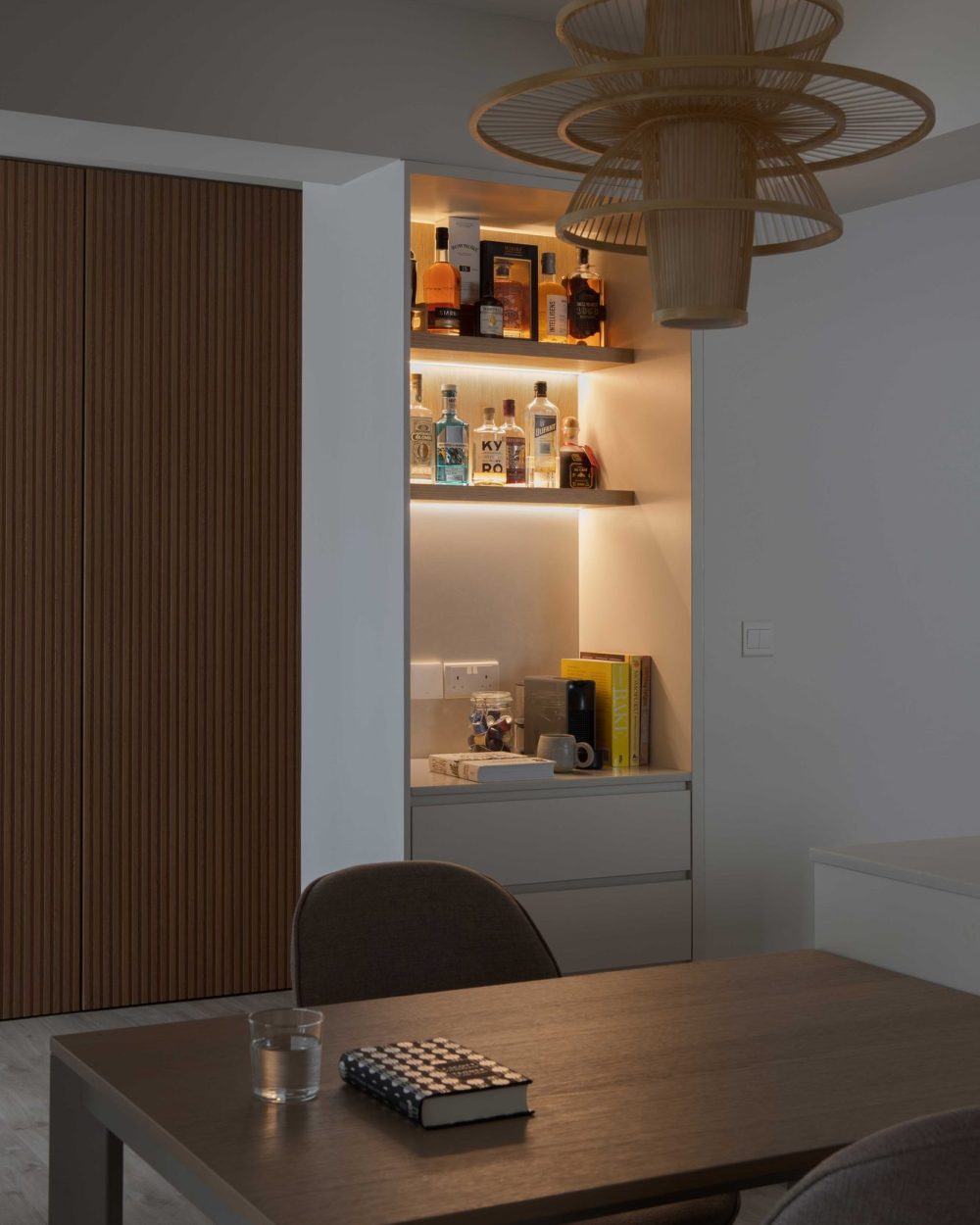 A run of backlit open shelving displays spirits and glassware, tucked into a niche beside the dining table.