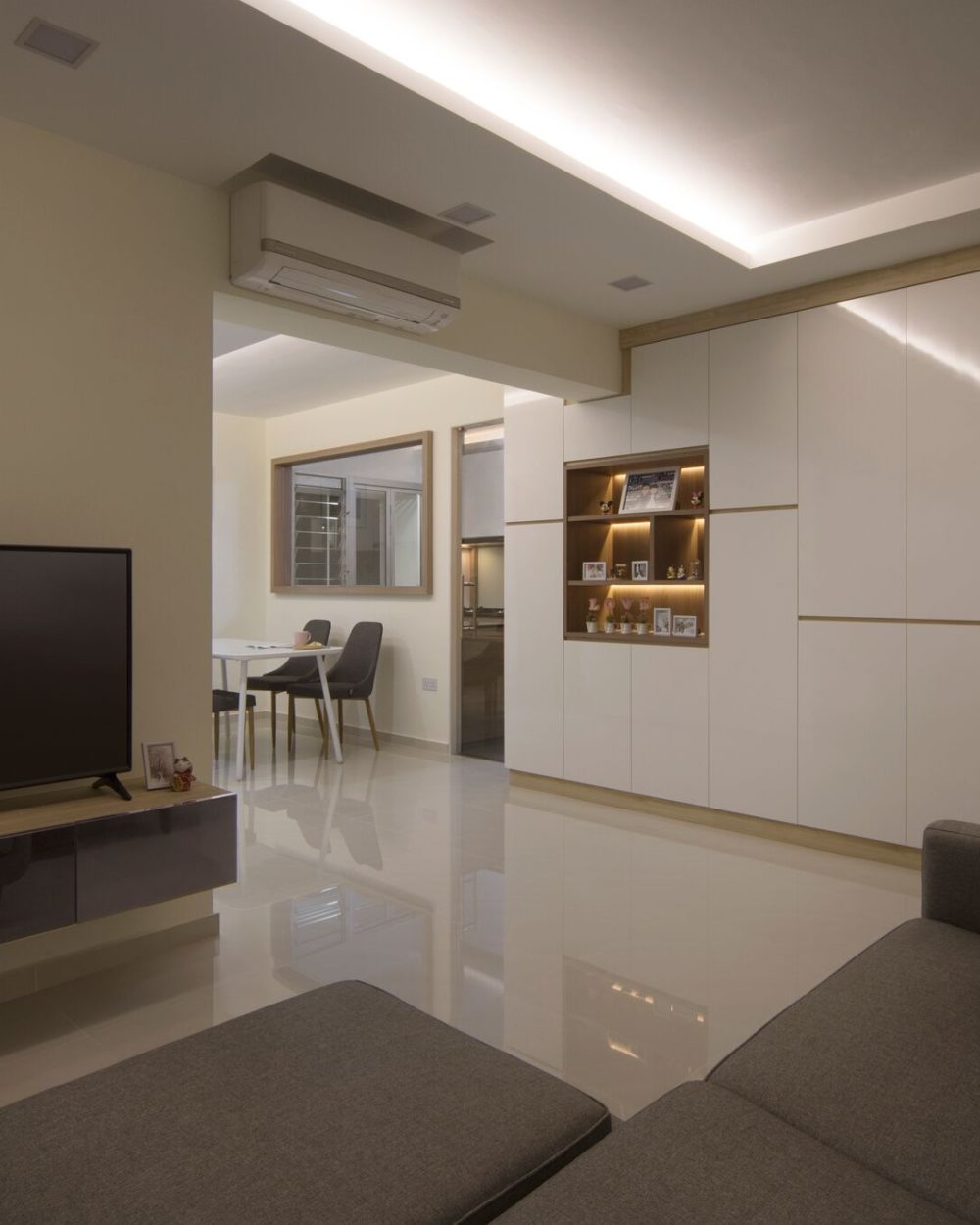 Full-height white cabinetry with a warm timber-lined niche displays keepsakes and photos, running from the entryway into the living room.