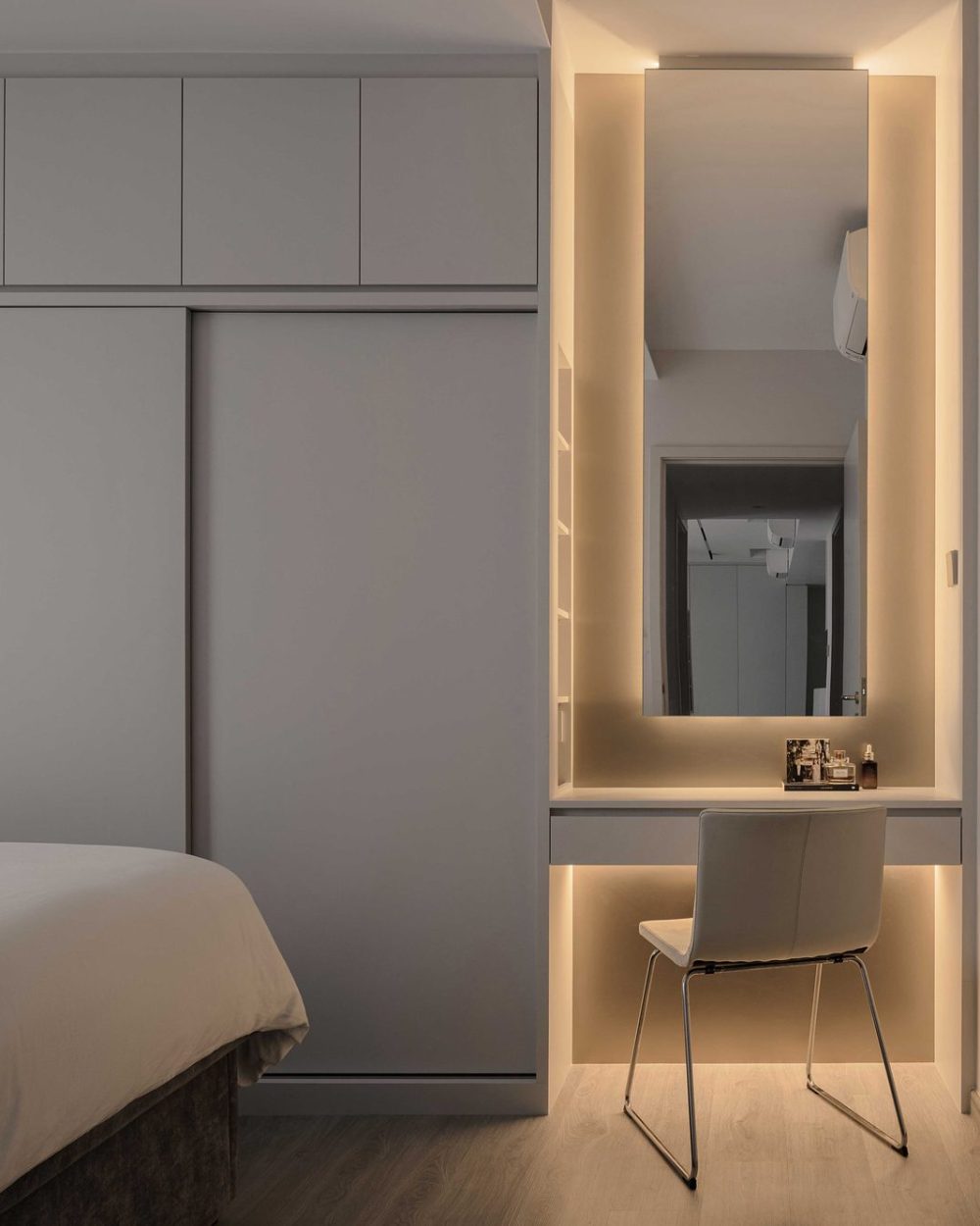 A tall backlit mirror and built-in desk create a dedicated dressing nook just off the bedroom.
