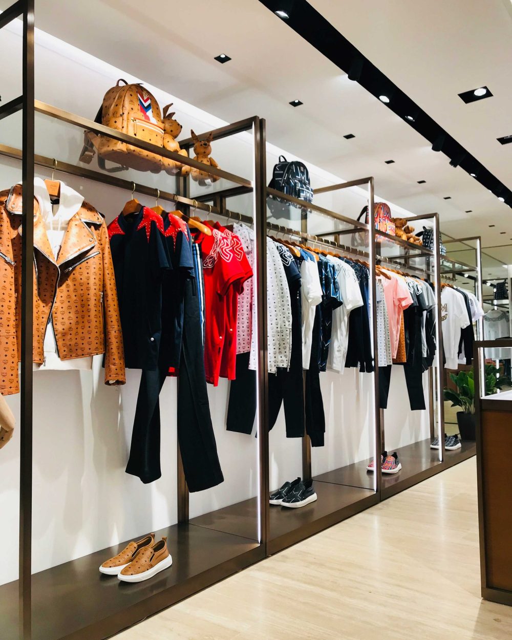 A clothing rack of graphic t-shirts and track pants with a backpack and plush toy above.