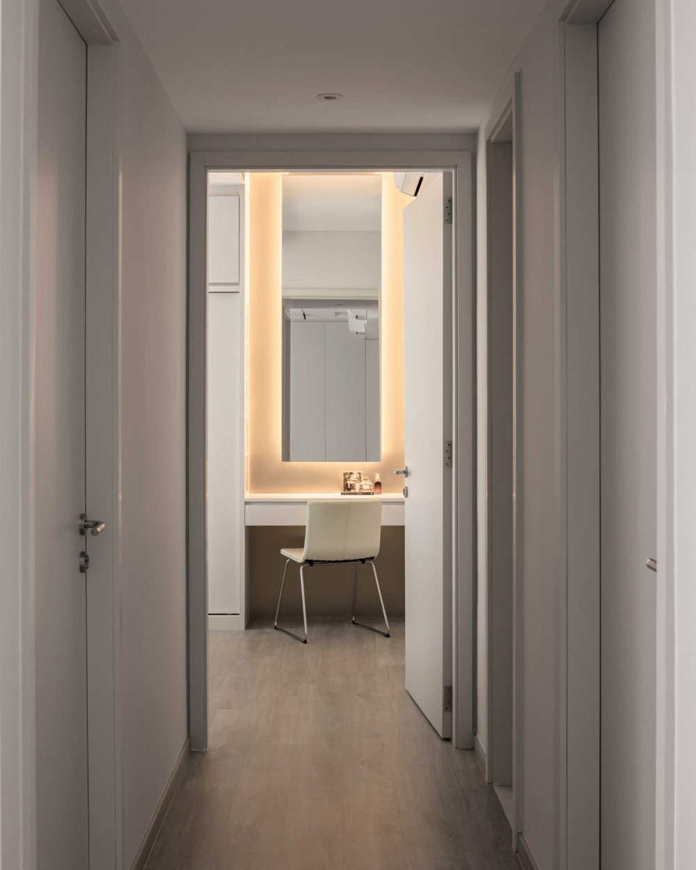 A warm strip of light guides the way down the hallway to the bedroom's backlit dressing nook.