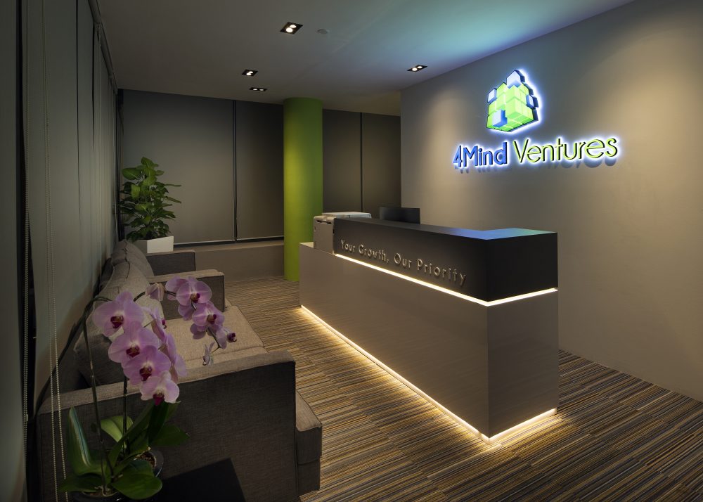 An illuminated logo and tagline mark the reception desk, framed by a lime-green feature column and striped carpet flooring.