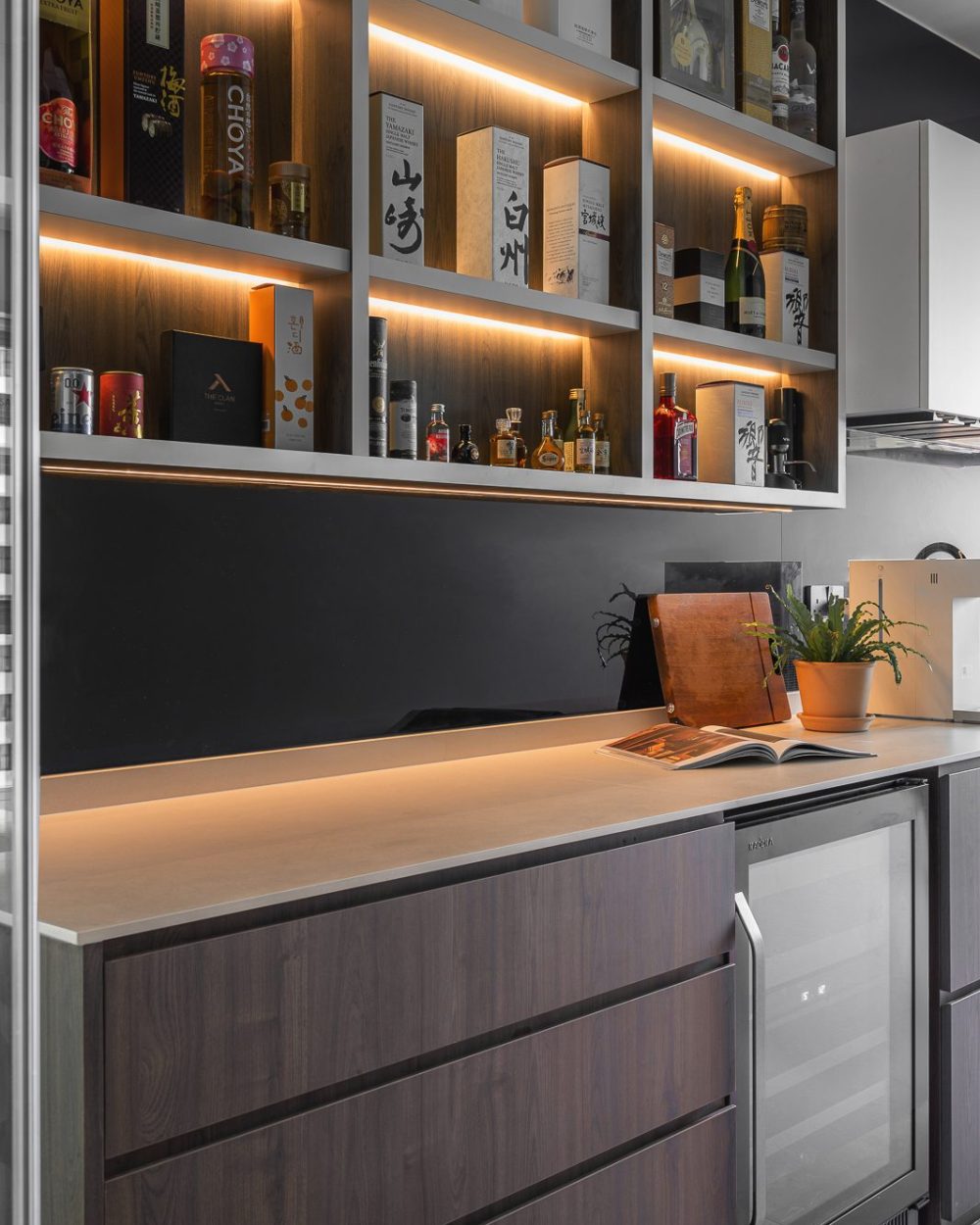 A dedicated bar shelf displays an extensive whisky and spirits collection, each bottle lit from within against a black backsplash.