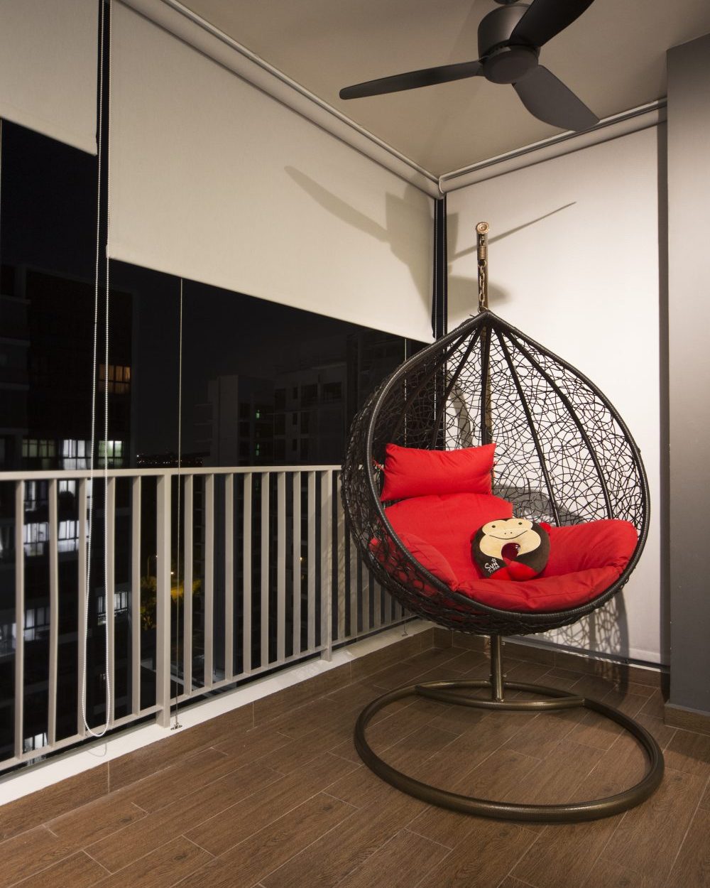A hanging egg chair with red cushions turns the balcony into a private perch, looking out over the city skyline at night.