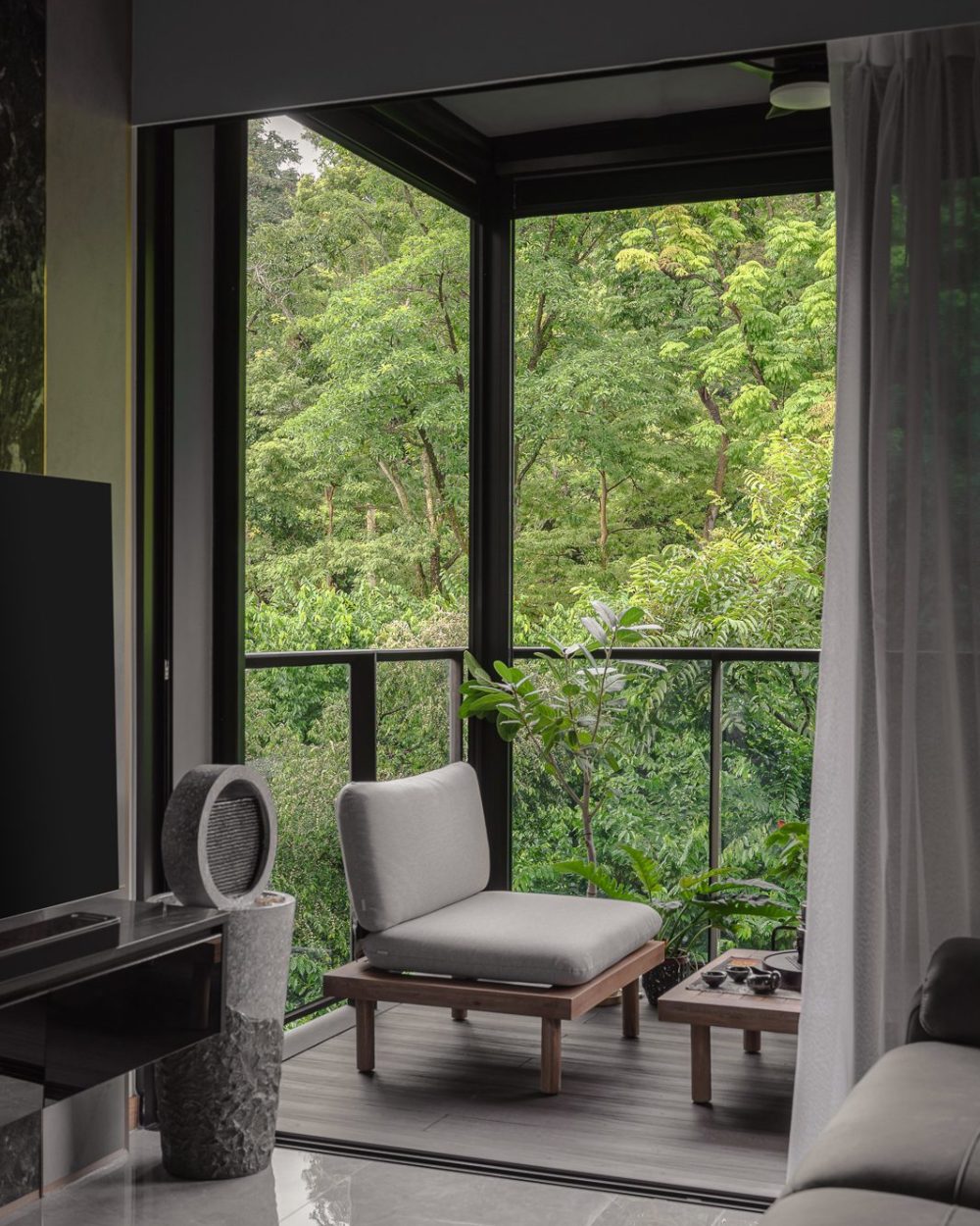A low lounge chair and tea table look out over a canopy of trees, turning the balcony into a private retreat.