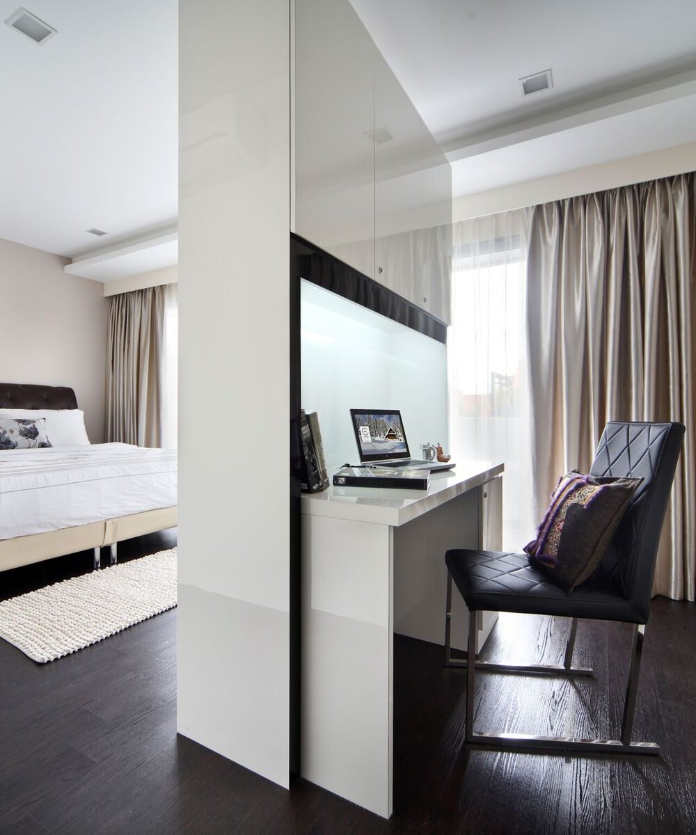 A glass-fronted display desk sits beside a tufted dark headboard, with floor-to-ceiling gold curtains framing the window.