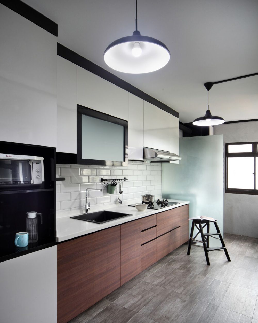White subway tiles and gloss cabinetry pair with walnut-toned lower units and black trim detailing, finished with two pendant lights over the counter.