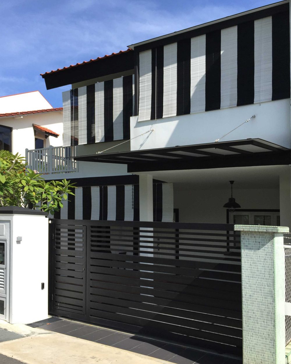 Vertical black-and-white bamboo blinds wrap the upper storey's window bays, giving the facade a bold, graphic pattern against the white render below.