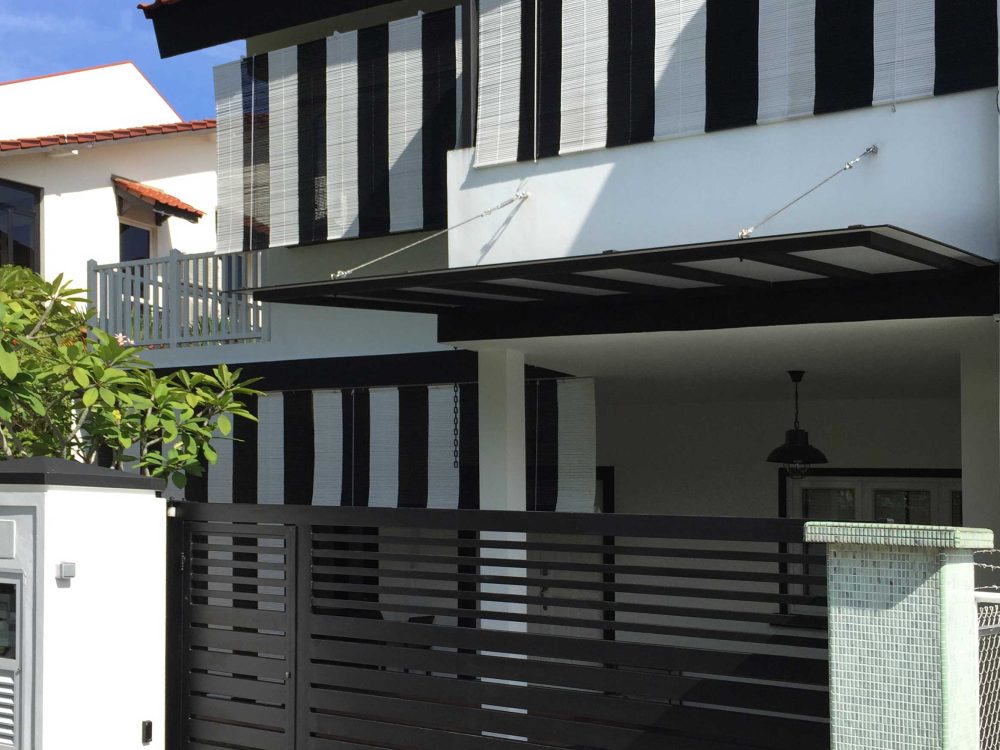 Vertical black-and-white bamboo blinds wrap the upper storey's window bays, giving the facade a bold, graphic pattern against the white render below.