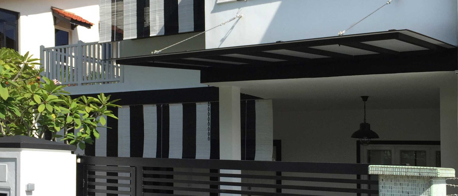 Vertical black-and-white bamboo blinds wrap the upper storey's window bays, giving the facade a bold, graphic pattern against the white render below.