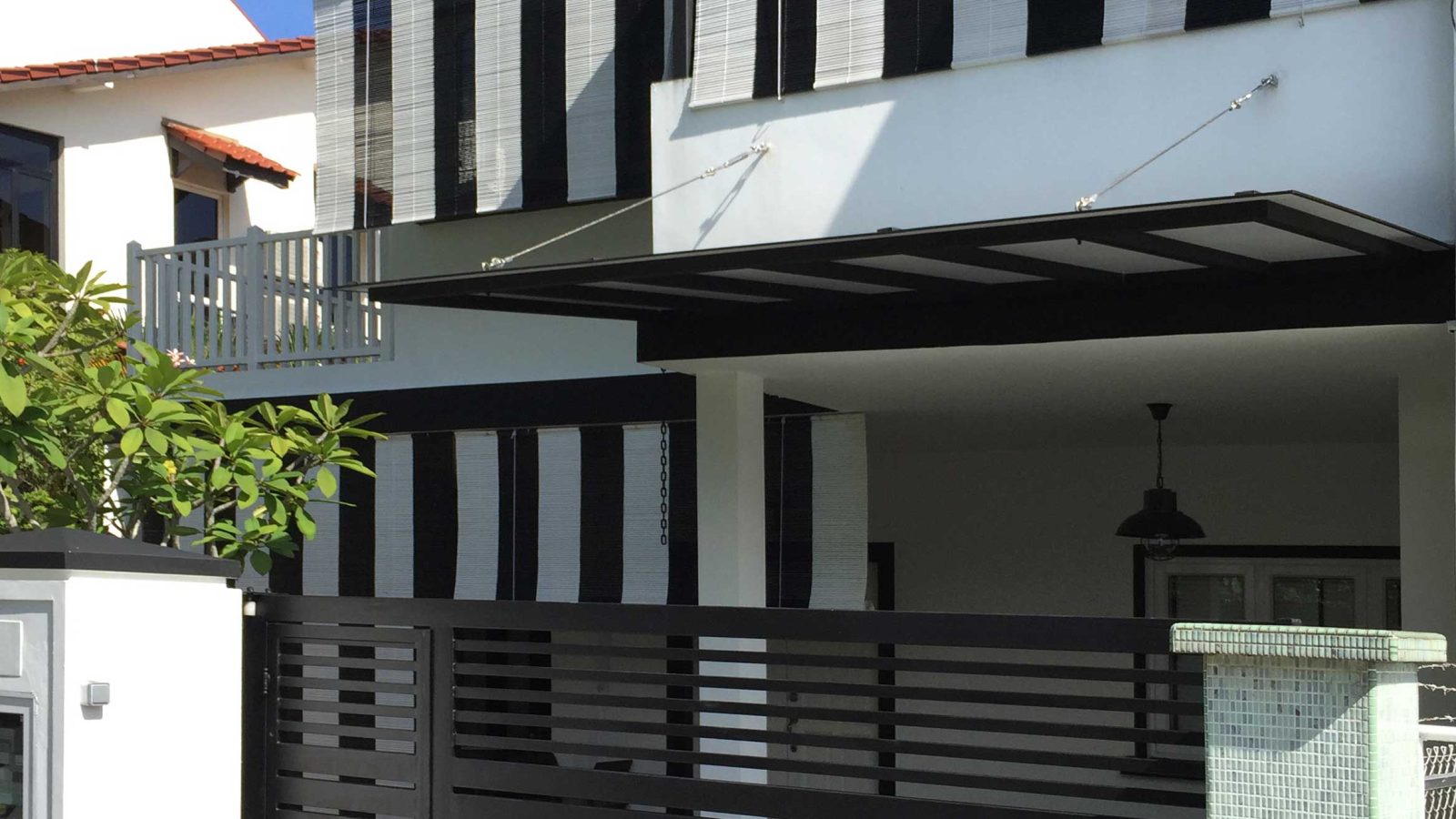 Vertical black-and-white bamboo blinds wrap the upper storey's window bays, giving the facade a bold, graphic pattern against the white render below.