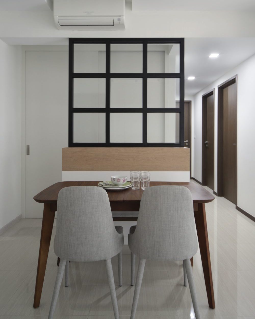A nine-pane black-framed glass partition divides the dining area from the bedroom corridor, letting light pass through while keeping each zone distinc