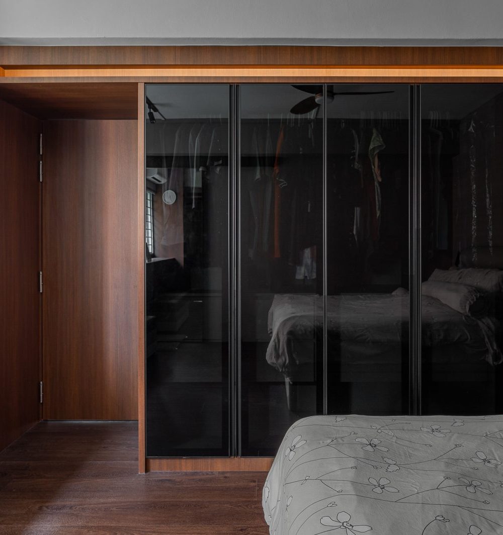 Full-height black glass wardrobe doors reflect the bedroom softly, keeping the room's storage sleek and understated.