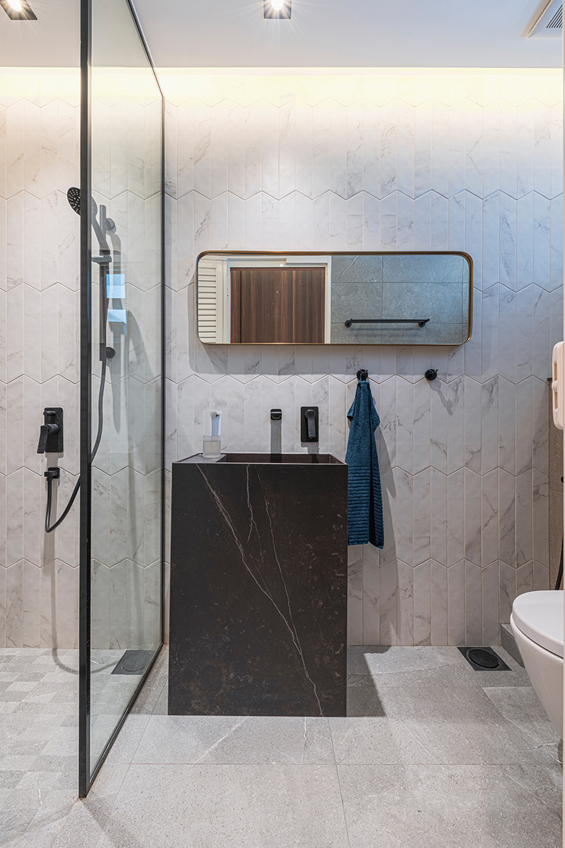 A closer look at the black pedestal sink and framed mirror, set against the same herringbone marble backdrop.