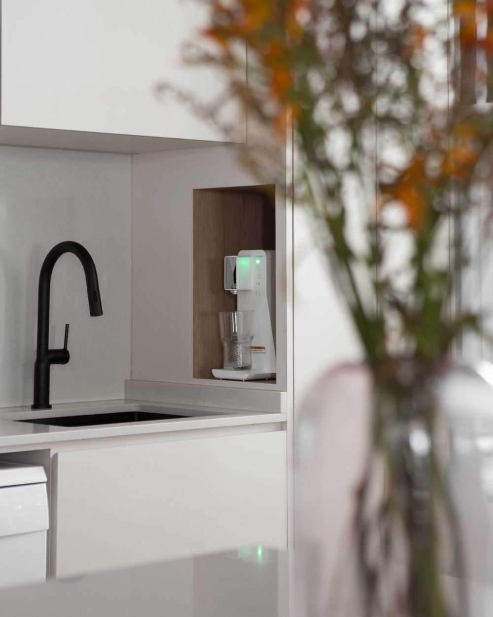 Matte black tapware pairs with a built-in filtered water dispenser, niched into warm timber-lined joinery.