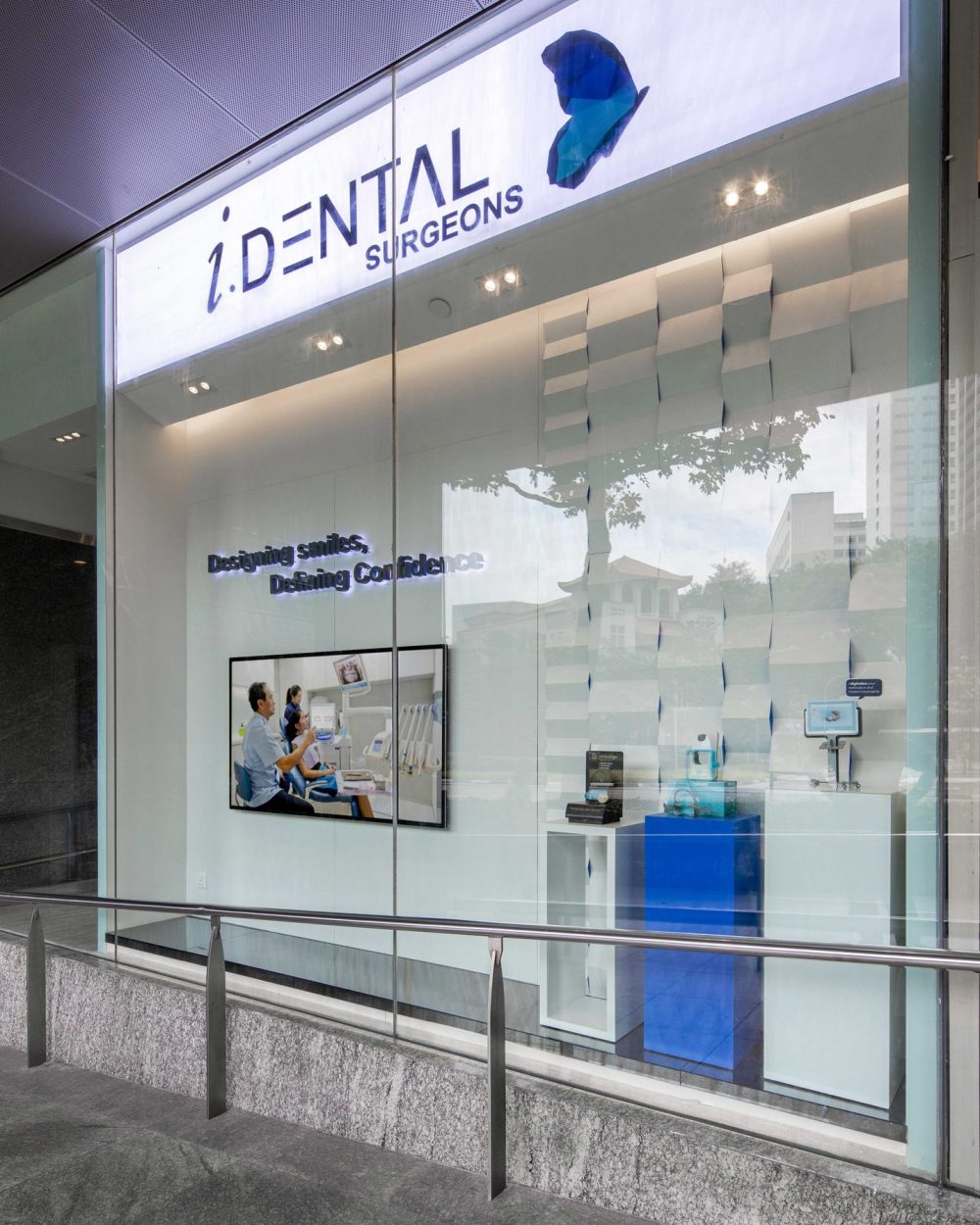 A folded, faceted wall panel and backlit logo announce the practice from the street, paired with a video display introducing the team.