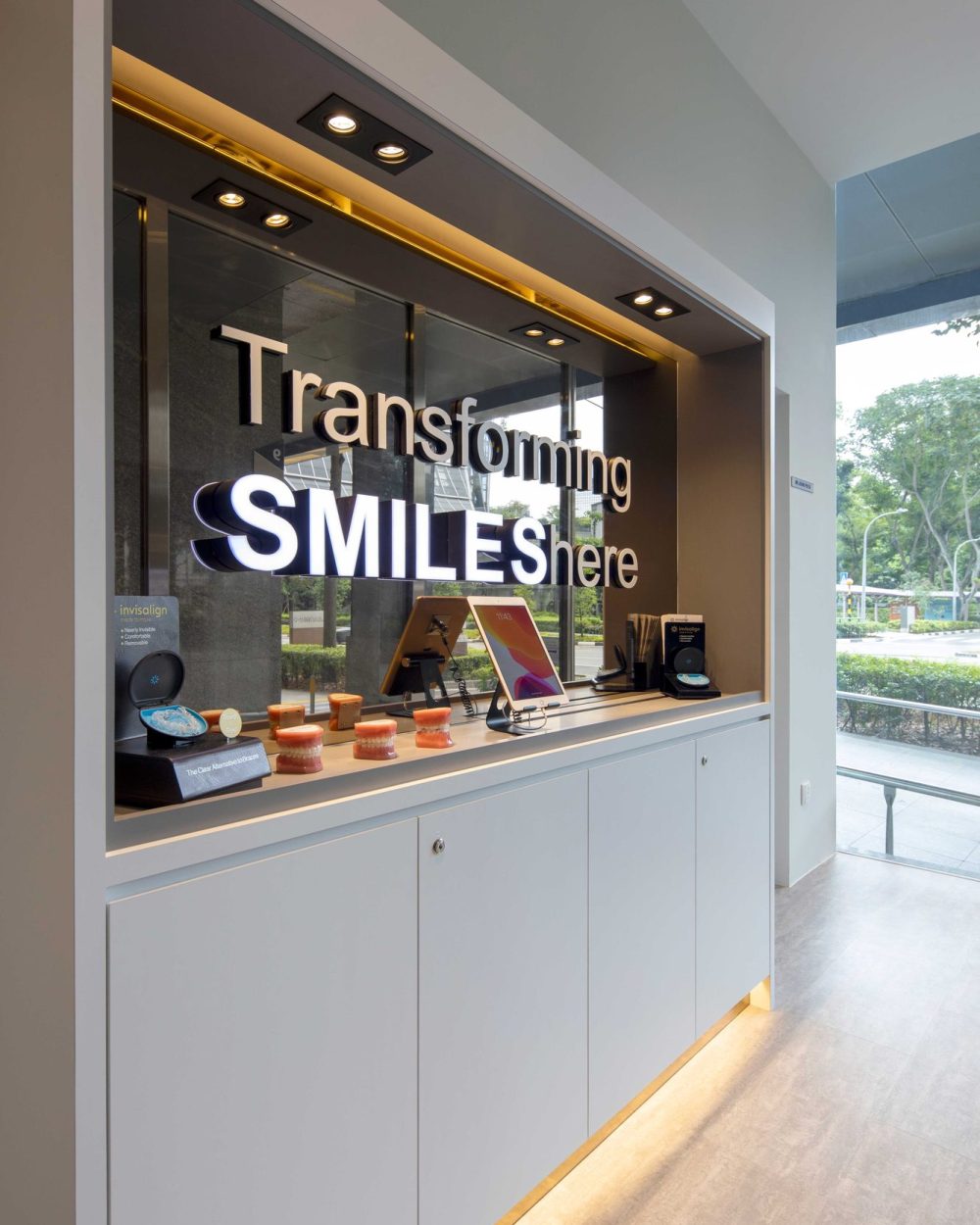 Backlit signage spelling out 'Transforming Smiles Here' anchors a consultation display featuring Invisalign models and digital screens.