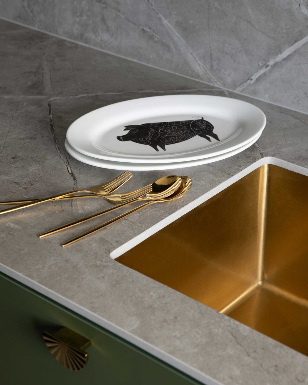 A brushed brass sink and matching gold cutlery bring warmth to the kitchen, paired with playful pig-print serving plates.