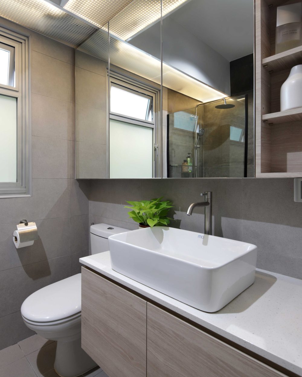 A full-width mirrored cabinet and warm timber vanity keep the common bathroom bright, with a glimpse of the glass shower reflected behind.