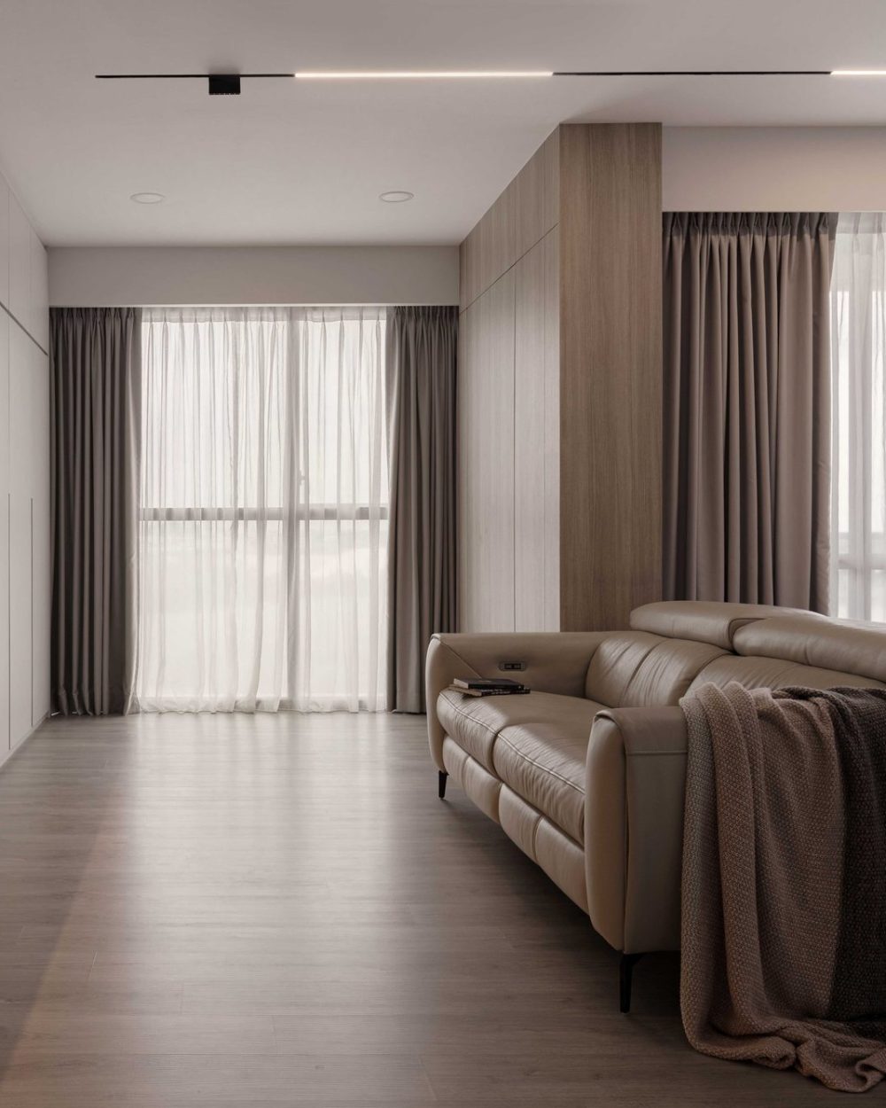 Sheer and blackout curtain layers soften the living room's floor-to-ceiling windows, paired with a taupe leather sofa.