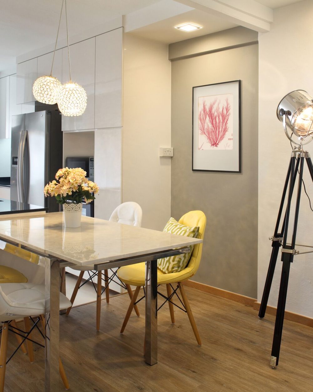 Yellow leather dining chairs and a coral botanical print add colour to the dining corner, framed by a tripod spotlight floor lamp.
