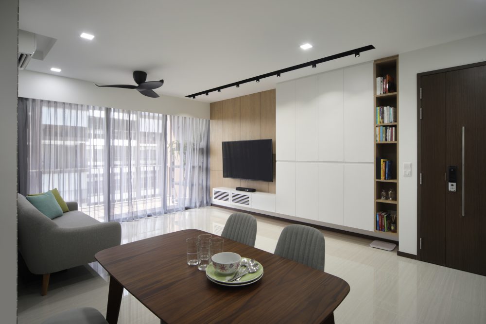 Sheer curtains soften the light from the balcony, with the dining area and its black-framed glass partition visible just beyond.