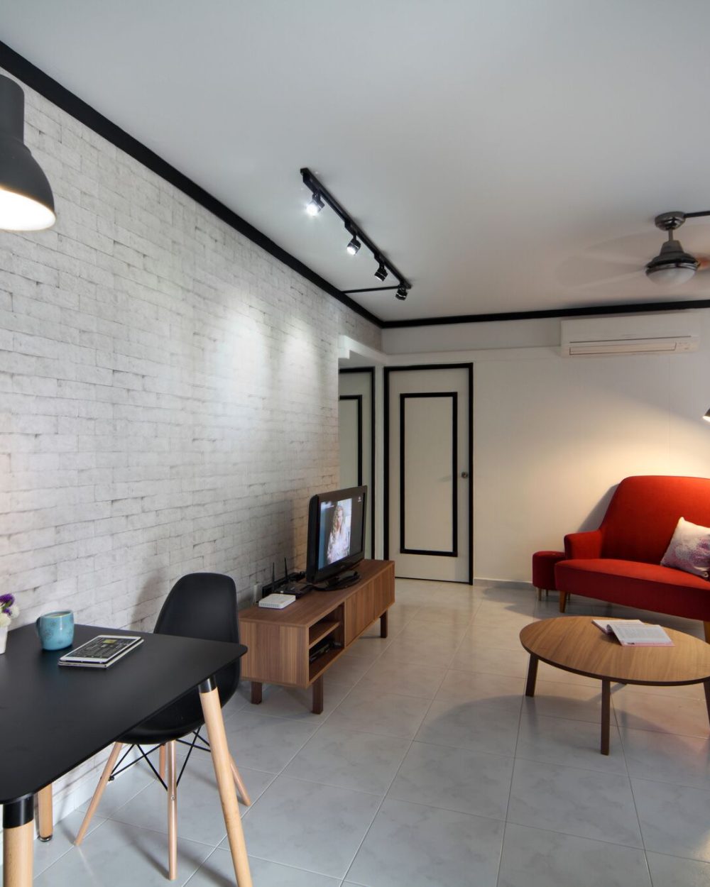 The same white brick-effect wall extends into the seating area, where a red accent armchair and charcoal sofa sit around a round wood coffee table und