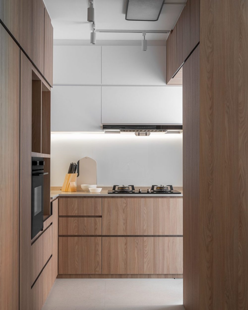 A gas hob and glass splashback sit within a crisp white-and-timber kitchen bay, styled simply with a knife block and bowls.