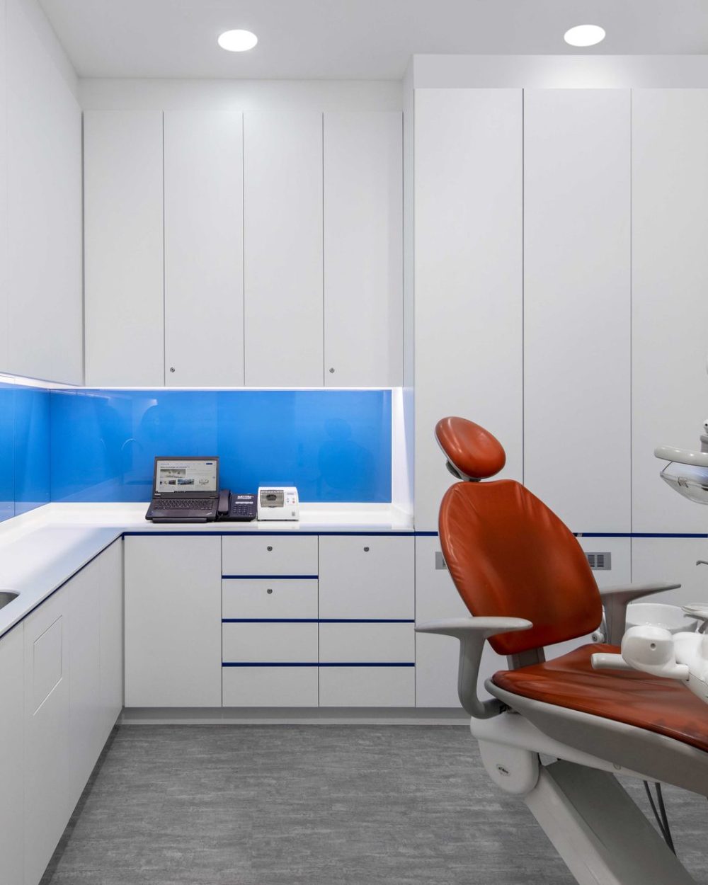 A vivid blue glass backsplash and orange upholstered dental chair give this treatment room a bold, clinical-yet-approachable character.