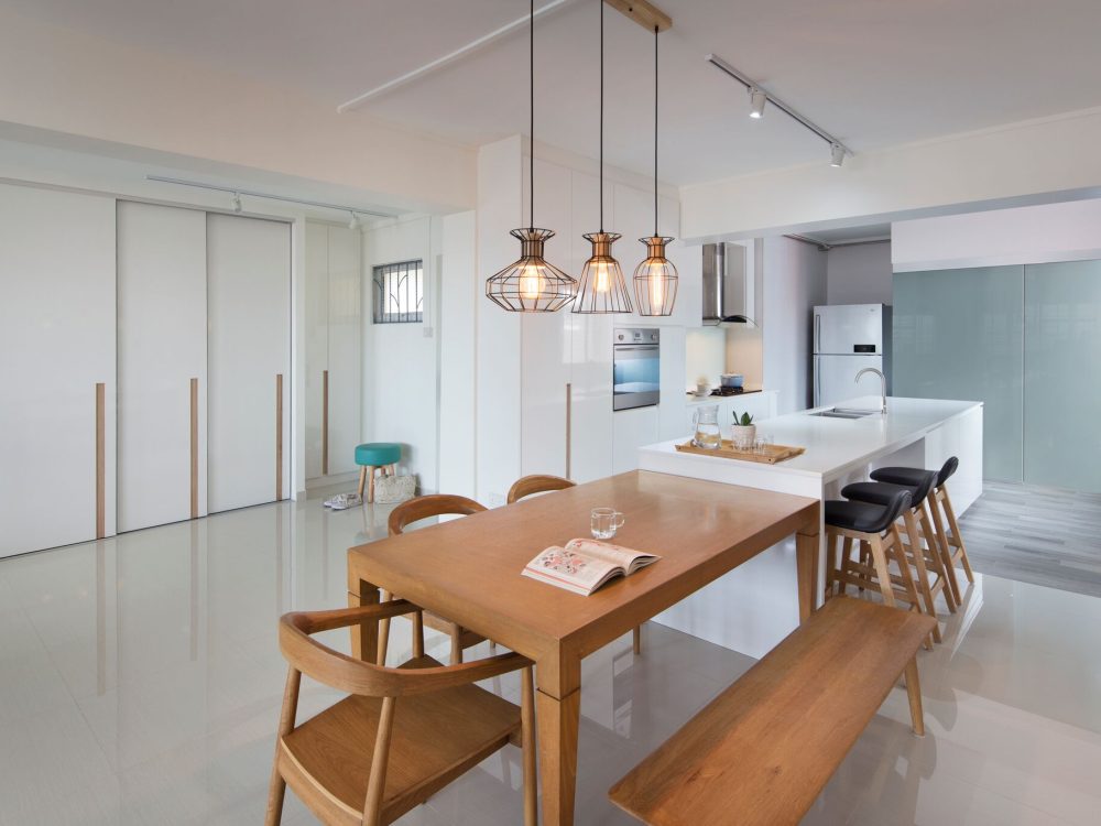 Three wire cage pendants hang over a bench-seated dining table, with a glossy white kitchen island and black bar stools completing the open-plan space