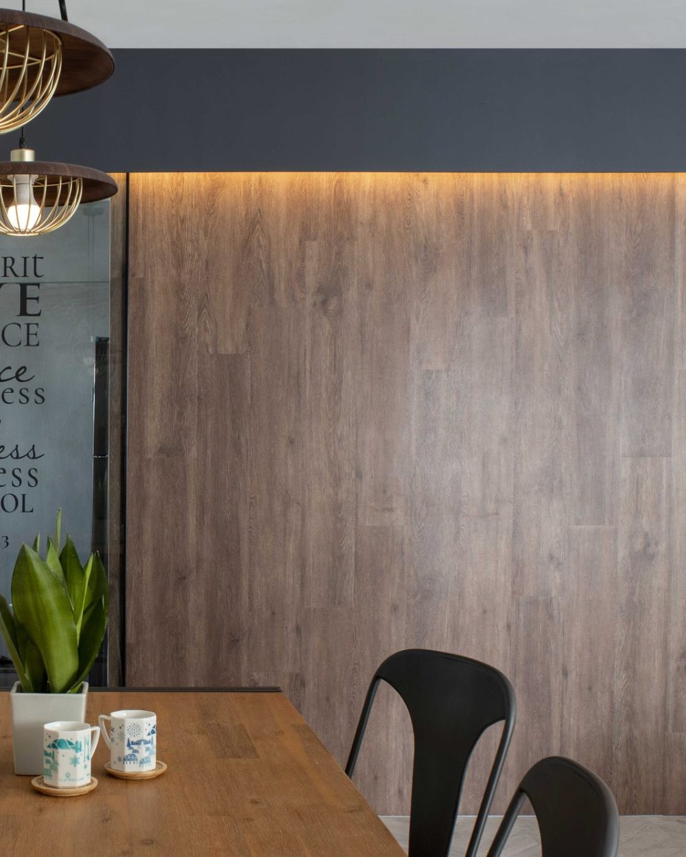 Timber-and-brass cage pendants hang over the dining table, with the scripture door and kitchen visible just beyond.