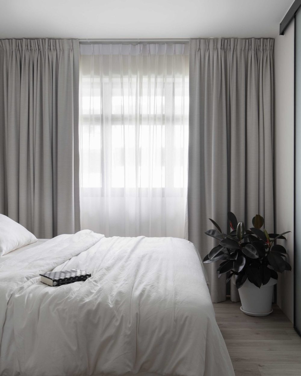 Floor-to-ceiling curtains and crisp white linens create a calm, hotel-like bedroom, with a frosted glass door leading to the wardrobe beyond.