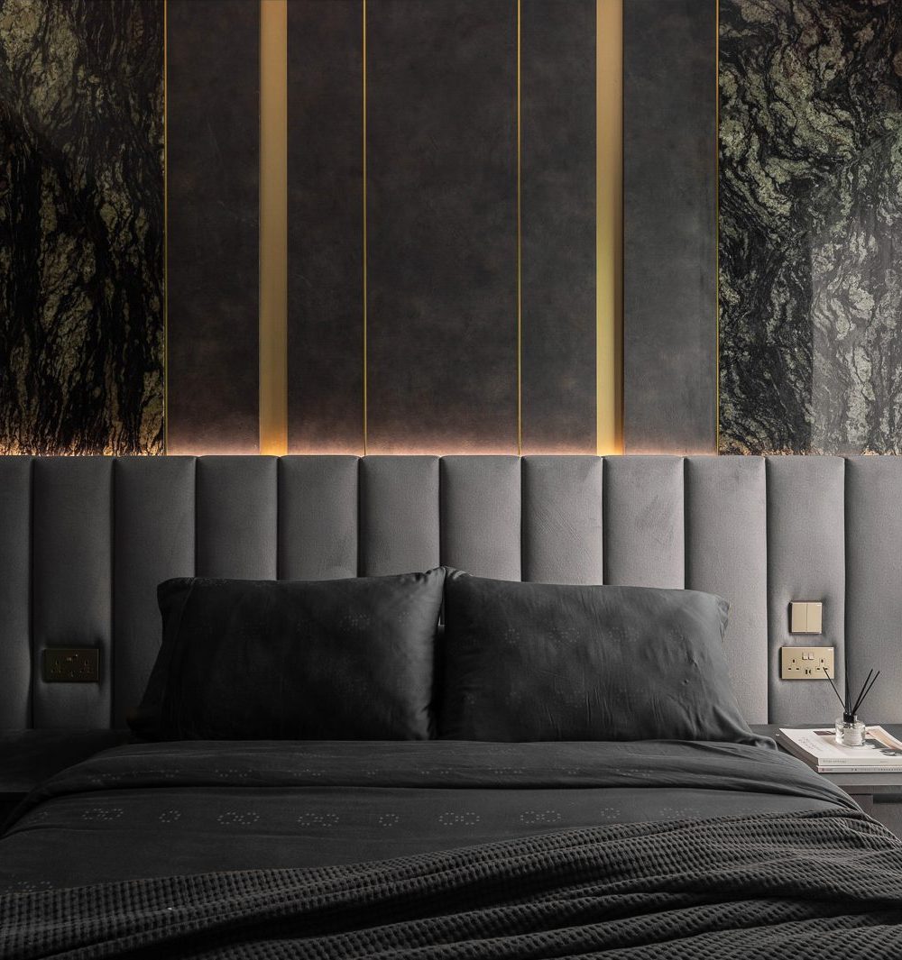 Vertical channel-tufted upholstery meets a backlit marble-and-brass panel above the bed, creating a rich, layered headboard wall.