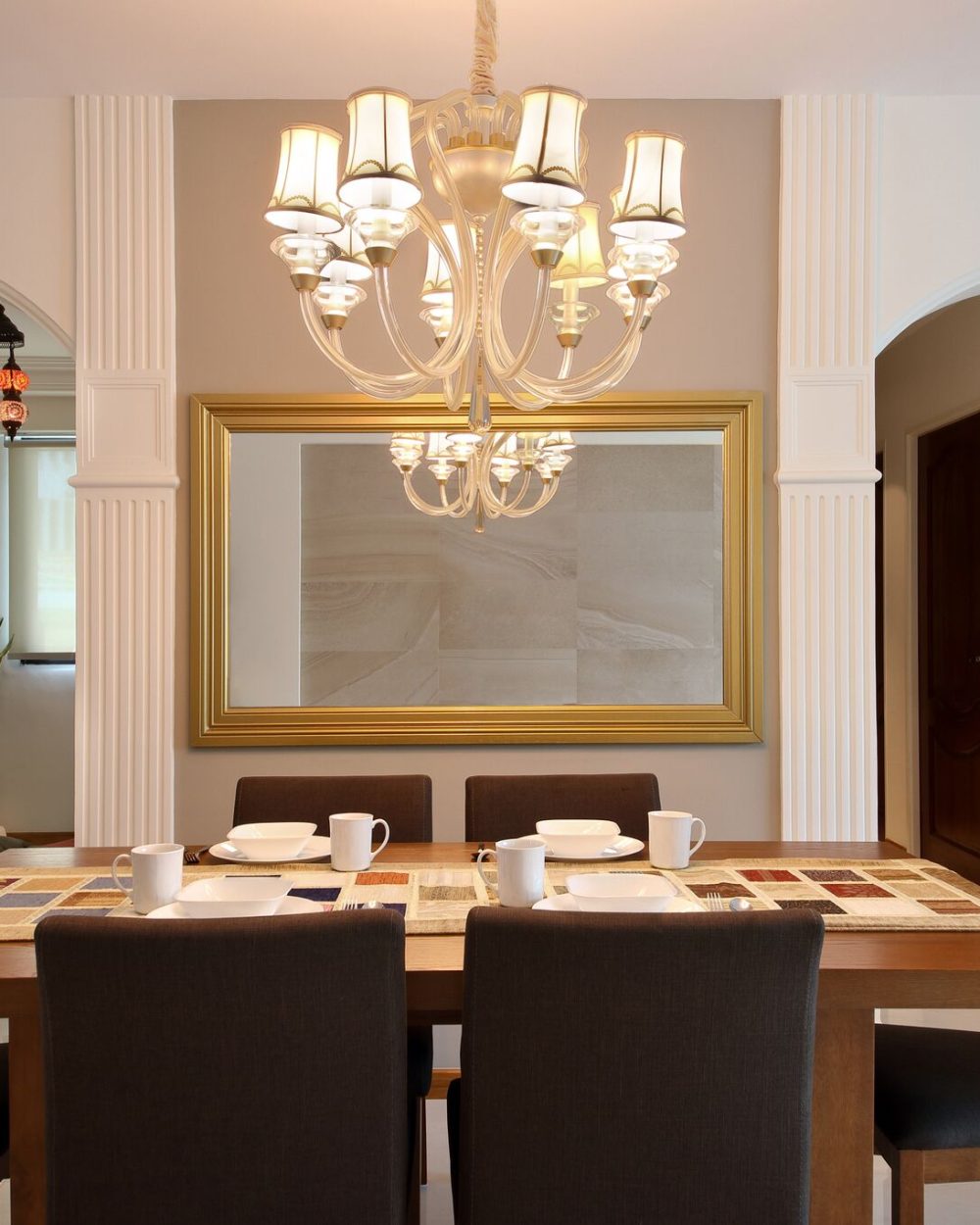 Fluted columns and arched openings frame a gold-edged mirror, with Moroccan pendant lanterns glimpsed in the corridor beyond.