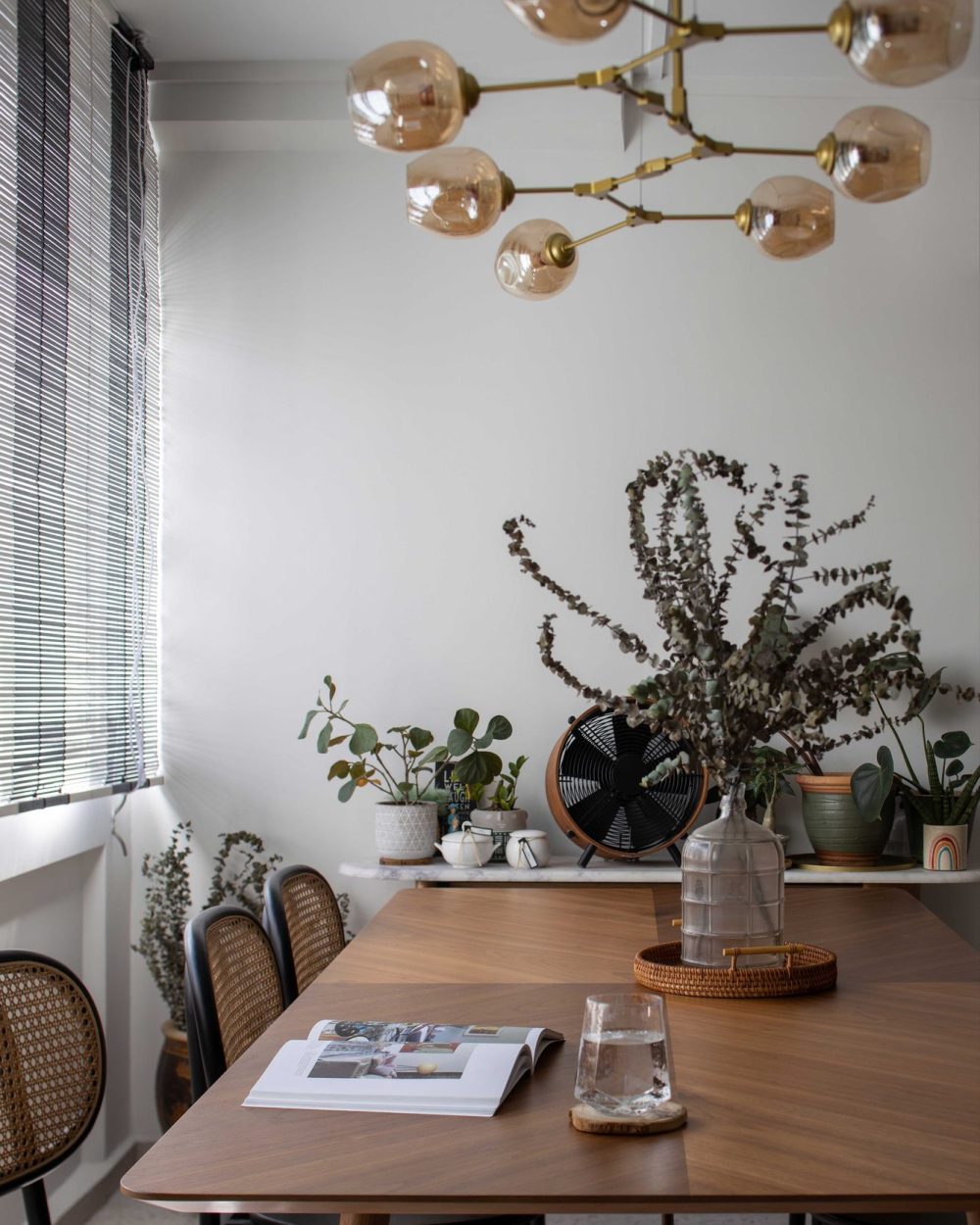 Amber glass globes catch the light beautifully against the dining room's striped black-and-white blinds and layered greenery.