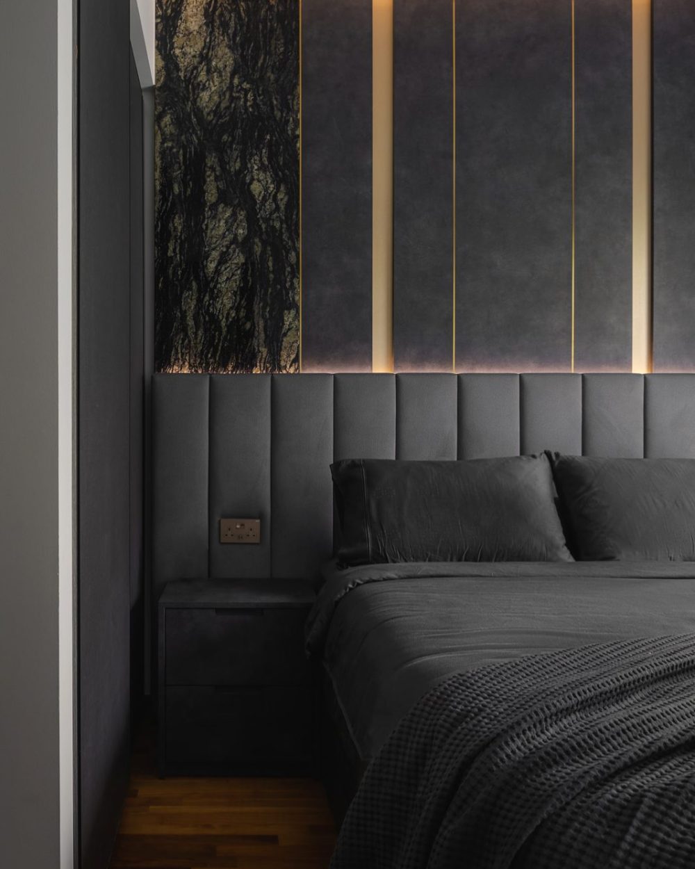 Brass strip lighting traces each marble and upholstered panel, adding a warm glow to the bedroom's dark palette.