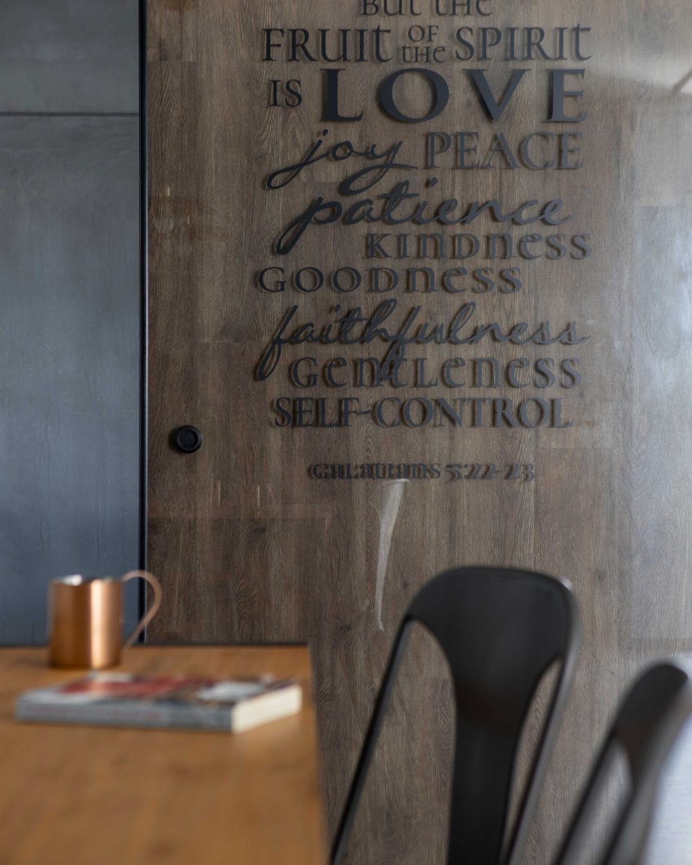 Every letter of the Galatians verse is individually cut into the timber-look door, backlit by a warm cove light above.
