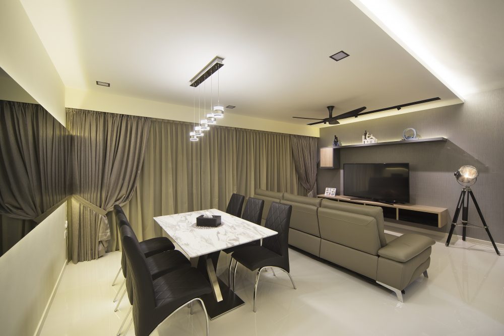A cascading cluster of pendant lights hangs over a marble-topped dining table, with quilted black dining chairs and the living room just beyond.