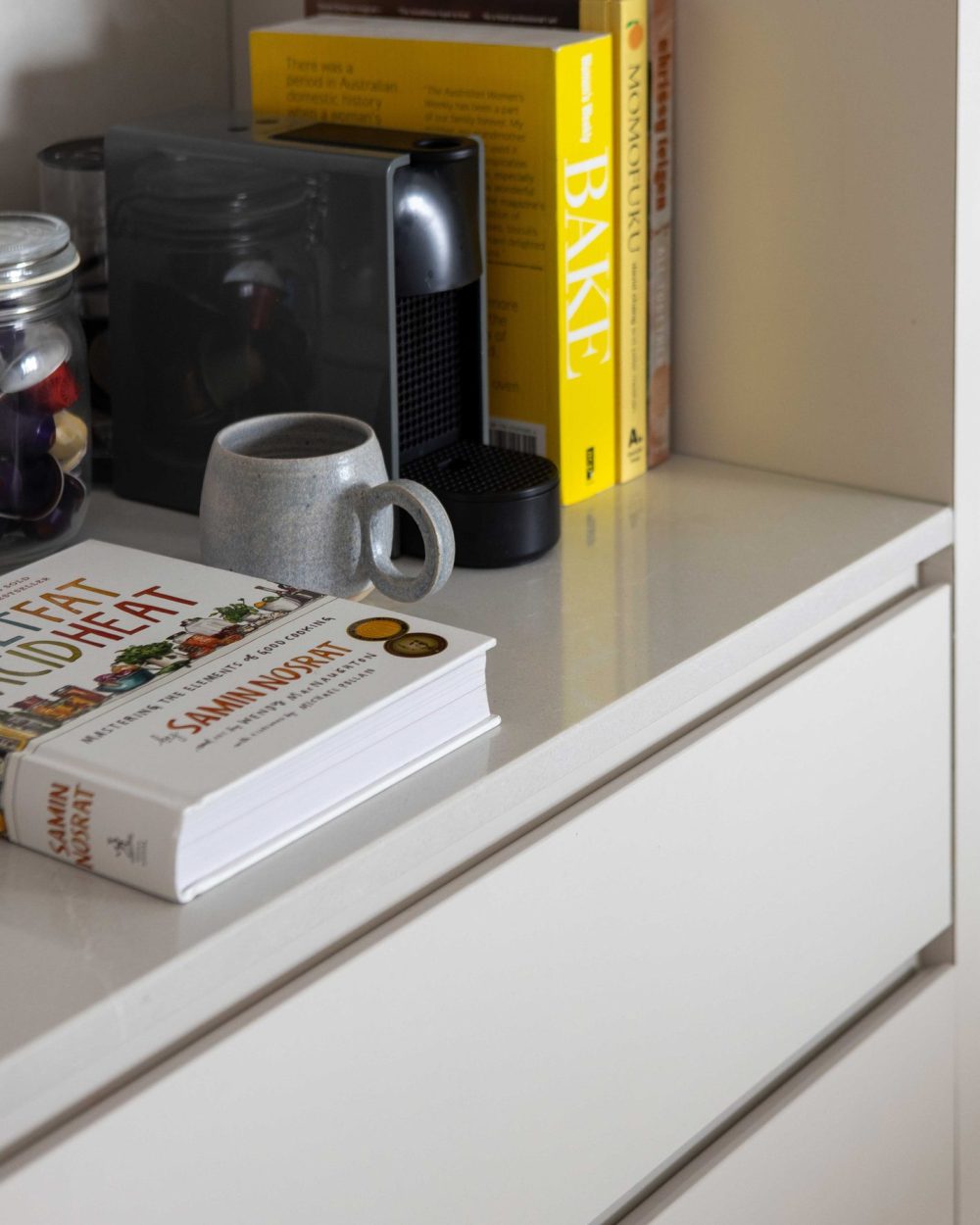 A built-in coffee machine and a stack of well-loved cookbooks sit on the bar nook's lower shelf, alongside a handmade ceramic mug.