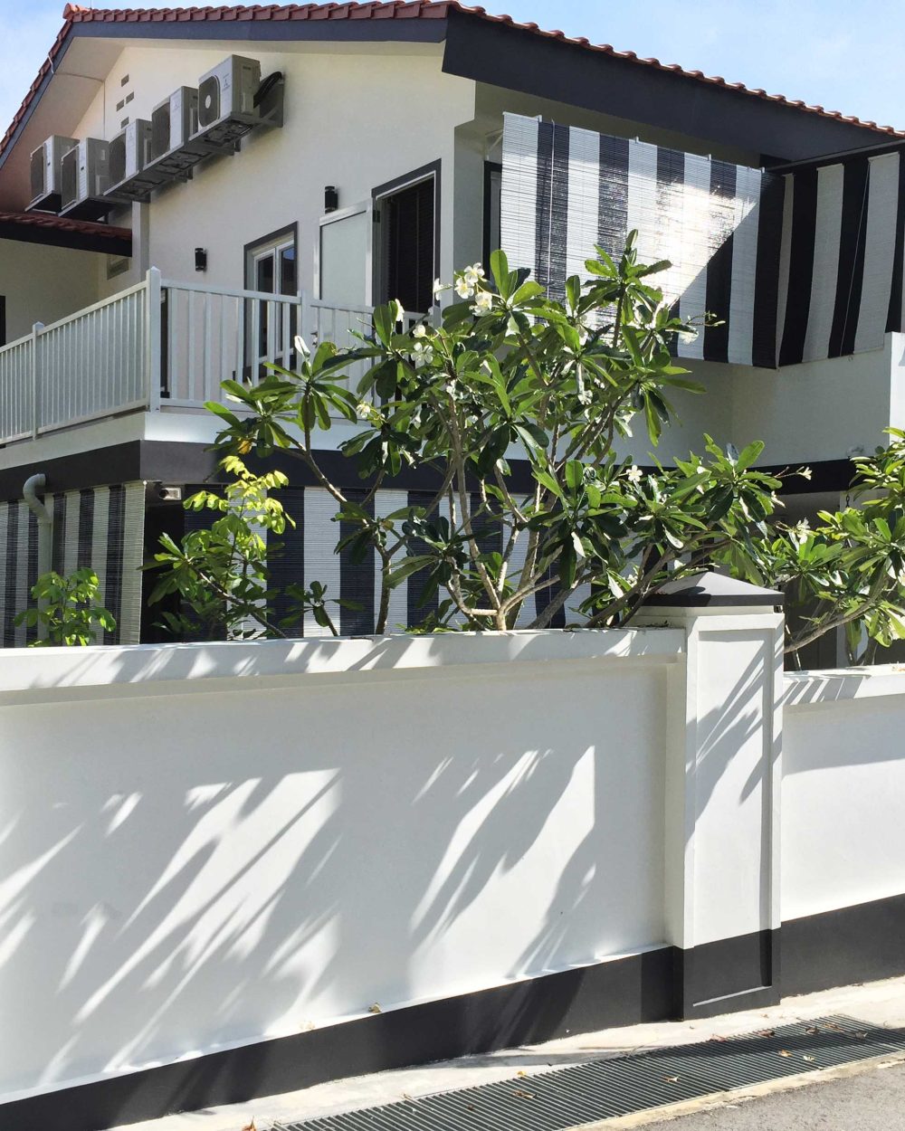 The black-and-white striping, charcoal roofline and white boundary wall carry through to the driveway gate, tying the whole frontage together.