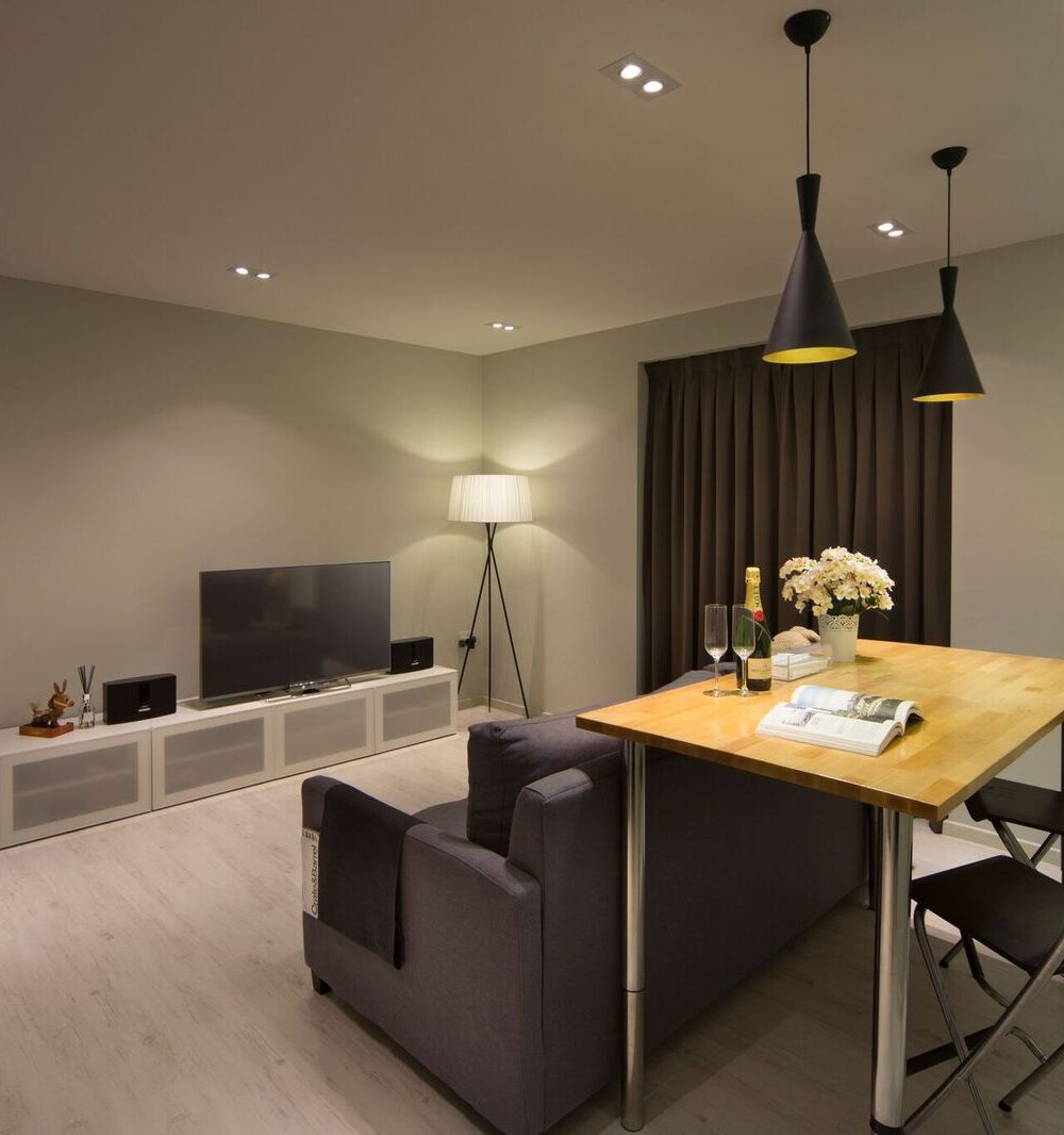 A folding dining table doubles the living room's function, paired with a charcoal sofa, black cone pendant lights and a slim media console.