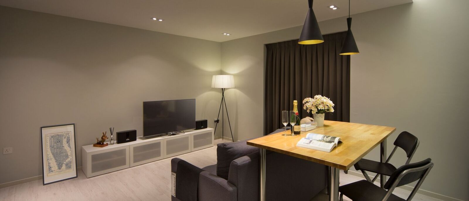 A folding dining table doubles the living room's function, paired with a charcoal sofa, black cone pendant lights and a slim media console.