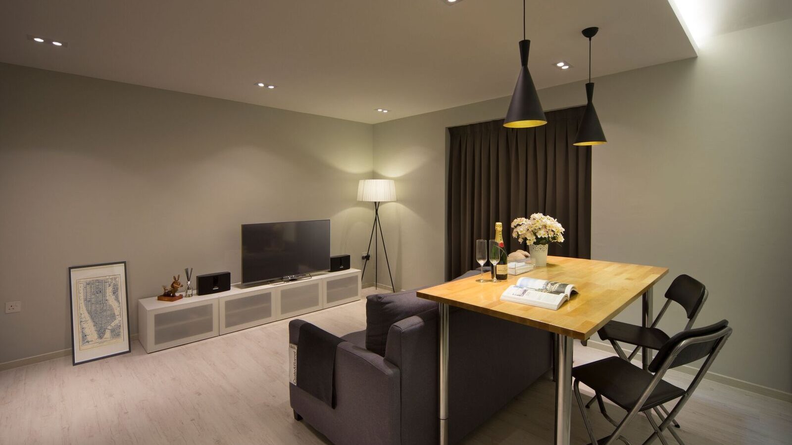 A folding dining table doubles the living room's function, paired with a charcoal sofa, black cone pendant lights and a slim media console.