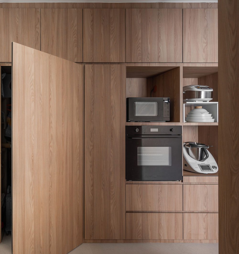 A door disguised within the same timber panelling opens to reveal the built-in appliance wall, keeping the kitchen's lines clean when closed.