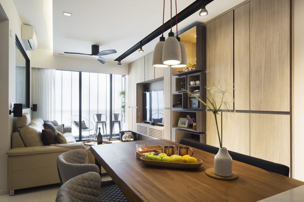 Three concrete pendant lights hang over a solid timber dining table, with the living area's display shelving continuing alongside.