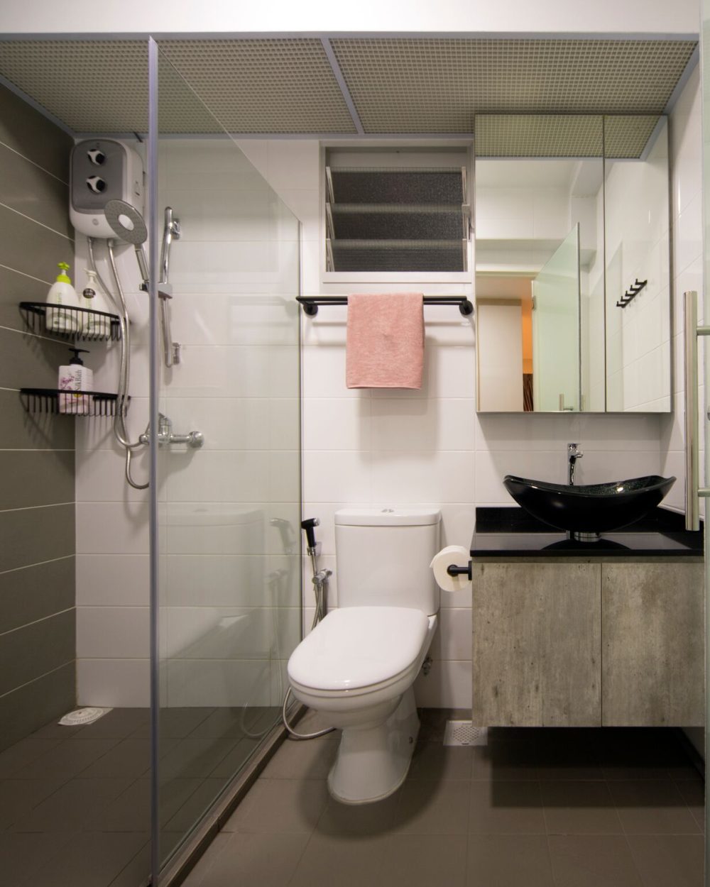 A black vessel sink and concrete-textured vanity pair with a glass-enclosed shower, finished with matte black fixtures.
